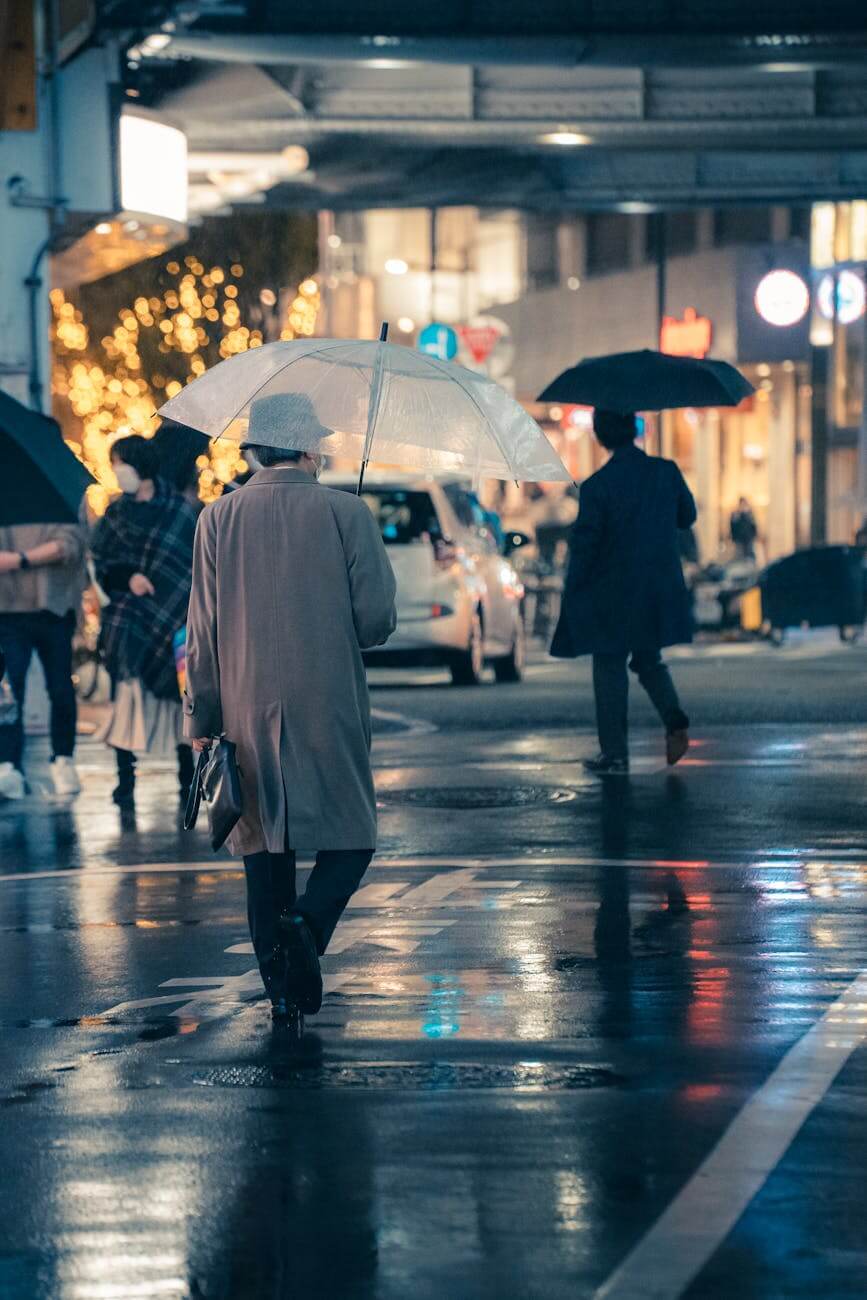 pedestrians walking with umbrellas along a wet street at dusk